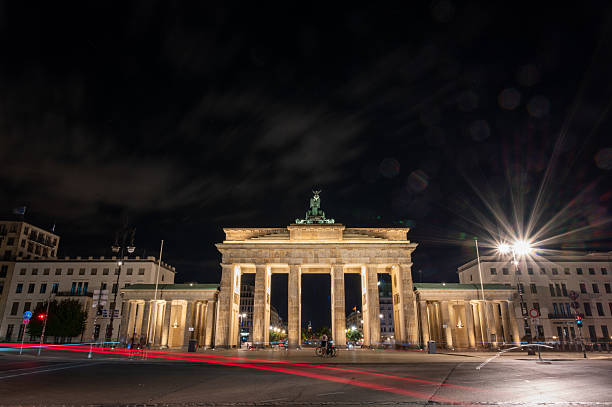 Berlin, germany, august 14, 2023. Brandenburg gate standing illuminated at night, featuring historic architecture with long exposure car light trails. Travel destination.