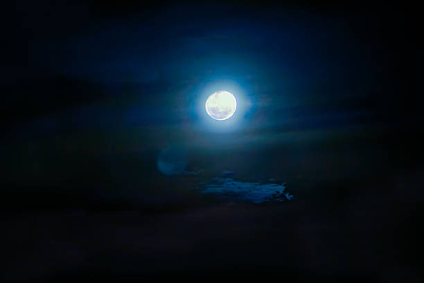 A luminous full moon shining through a dark, atmospheric night sky with soft clouds and a subtle blue halo effect