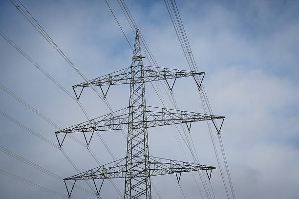 Steel lattice electricity pylon supporting multiple power lines, set against a wide sky with soft clouds, illustrating modern energy distribution.