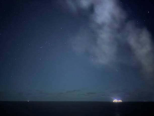 Cruise ship illuminates the dark ocean while sailing at night, captured under a vast sky dotted with stars and soft clouds, symbolizing travel, vacation, and distant adventures