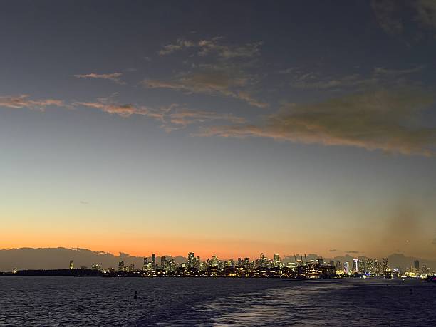Miami, Florida, skyline illuminating along the coast during twilight, showcasing a vibrant urban landscape reflecting on the calm ocean waters at sunset in Miami-Dade County
