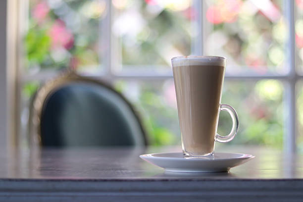Coffee latte in glass cup on wooden table near window