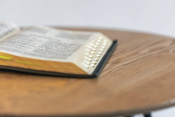Wide shot of an open Bible on a round wooden table in soft natural light with gentle bokeh. A peaceful mood for study, spiritual notes, and devotional focus.