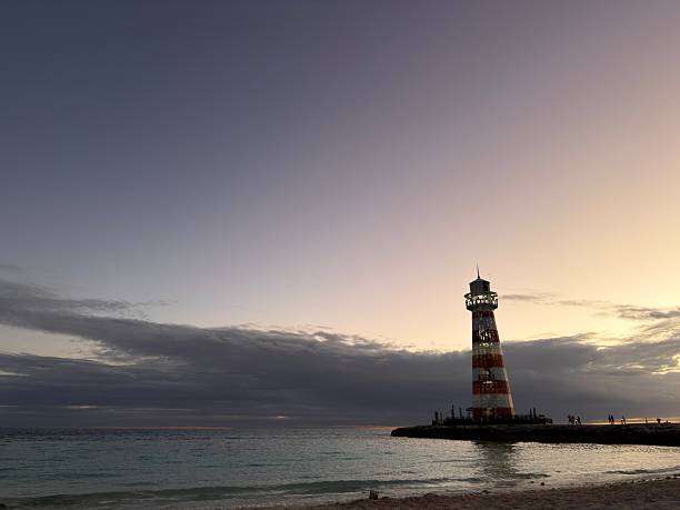 Ocean Cay lighthouse standing prominently on the small island against the vibrant hues of a sunset sky, with tranquil turquoise ocean waters gently lapping the sandy beach