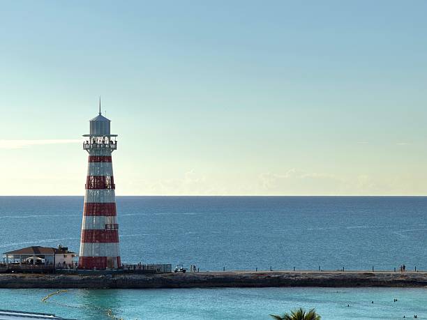 Ocean Cay lighthouse rising from the pier, marking the entrance to the colorful turquoise waters of the Bahamian island, with visitors enjoying the sunny tropical vacation destination