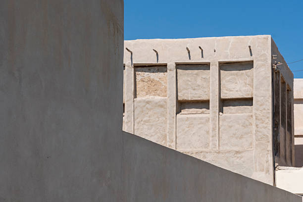 Traditional building displays characteristic Gulf architecture with wind tower and whitewashed walls at Muharraq Pearling Path, Bahrain. The well-preserved structure shows typical Arabian merchant house design. The historic building represents the traditional architecture that characterized Muharraq's pearling quarter, where wealthy merchants built elaborate houses using wind towers for natural cooling, demonstrating the architectural sophistication generated by pearling wealth, with such buildings documenting the prosperity and cultural refinement of Gulf pearling communities before petroleum economy transformed traditional society, making the preserved Muharraq pearling quarter exceptional for understanding pre-oil Gulf urban life.
