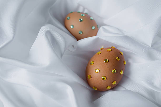 Easter eggs decorated with shiny colorful crystal rhinestones on a white silky tablecloth. New design vision on Christian Easter traditions, design ideas for holiday table.