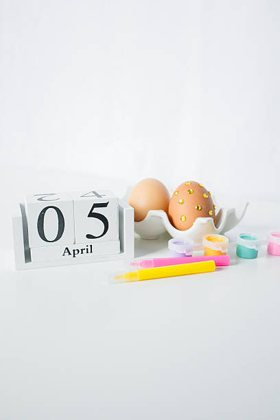 Christian Catholic Easter 2026 date on a wooden calendar with Easter eggs and paints for decoration on white background