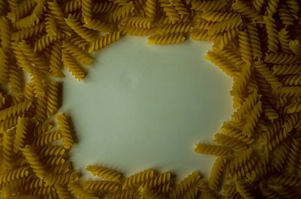 Uncooked fusilli pasta is arranged in a circular frame on a white surface, leaving empty space in the center for copy.