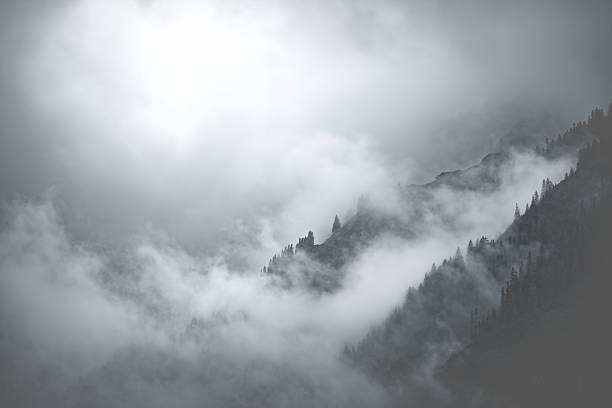 Landscape photography of the mountians of Tyrol with the sun coming through dense fog, monochrome, vertical