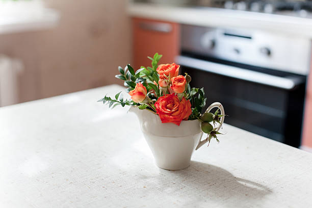 bouquet of fresh peony flowers in stovetop kettle on gas stove in home kitchen
