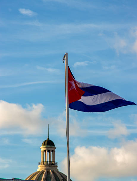 Cuban flag fluttering above Havana with historic dome silhouette under evening sky.
