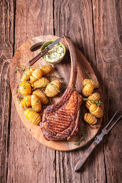Juicy Tomahawk Steak With Hasselback Potatoes and Herb Butter on Rustic Cutting Board
