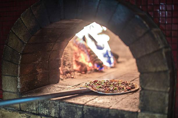 Wood-Fired Pizza Being Baked in a Traditional Stone Pizza Oven with Peel and Flames