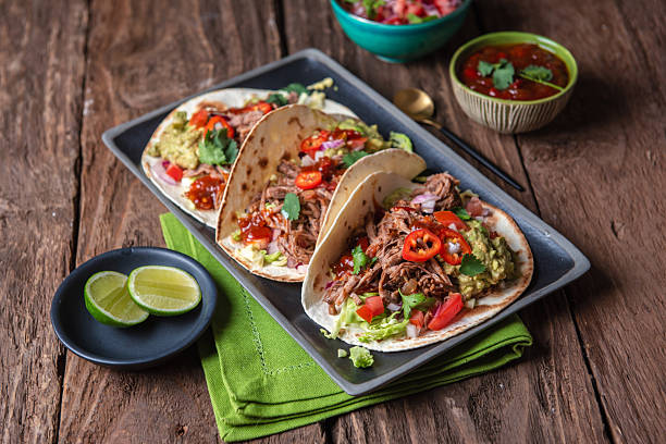 Pulled Pork Tacos With Guacamole, Salsa and Lime on Rustic Wooden Table