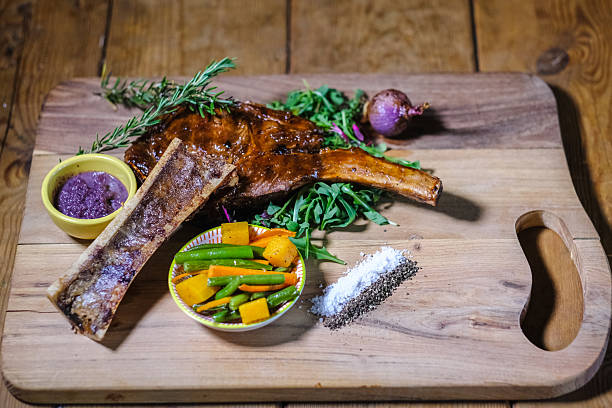 Grilled Bone-In Rib Steak With Roasted Vegetables, Sauces and Seasoned Salt on Wooden Board