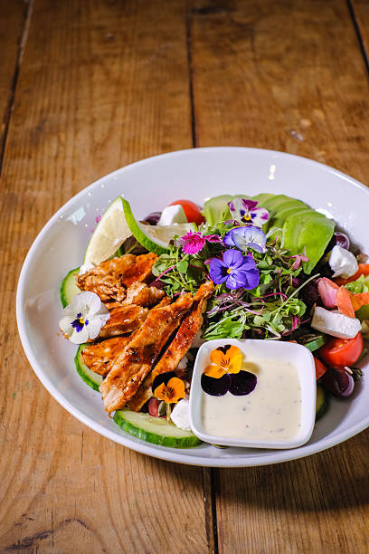 Grilled Chicken Salad With Avocado, Edible Flowers and Creamy Dressing on Rustic Wooden Table