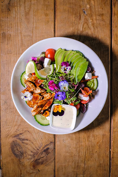Fresh Avocado Chicken Salad Bowl With Edible Flowers, Lime And Creamy Dressing On Rustic Table