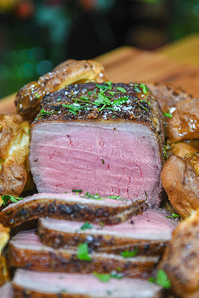 Sliced Medium-Rare Roast Beef With Yorkshires on Wooden Board Garnished With Parsley