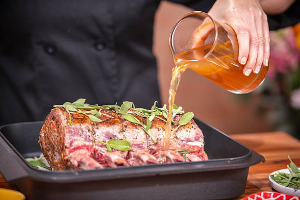Chef Pouring Gravy Over Herb-Crusted Roast Beef in Roasting Pan for Holiday Meal Preparation