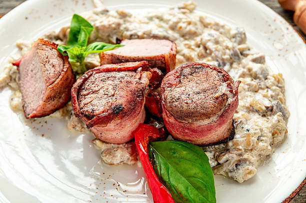 Grilled meat rolls with sauce and herbs on a white plate. Four pieces of grilled meat rolls are served with a creamy sauce. Fresh herbs add color and flavor to the dish.