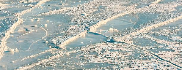 Blue ice sheet texture, intersecting skate grooves, curved scratch lines, scattered frost specks, small broken chunks, frozen rink surface background, winter cold abstract pattern, outdoor lake sheen.