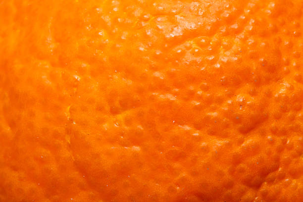 Close-up extreme macro shot of a vibrant orange fruit skin, showing detailed porous texture, oil glands, and bumpy organic surface. Perfect for background, food industry, or healthy lifestyle concepts.