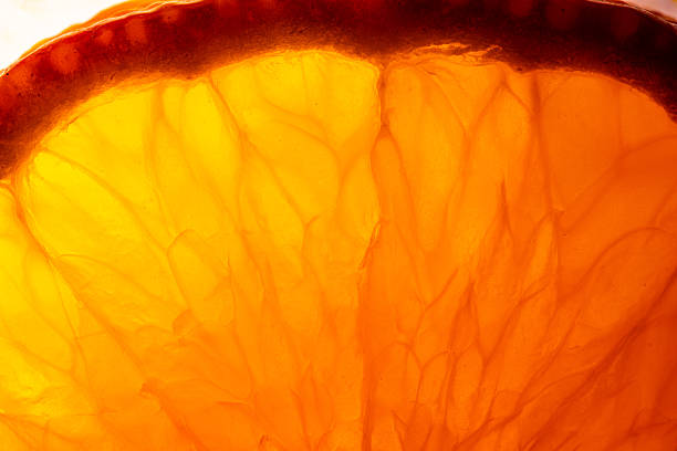 A detailed macro shot of a fresh orange slice, illuminated from behind to highlight the vibrant pulp, juice vesicles, and organic texture. Perfect for food, beverage, and healthy lifestyle themes.