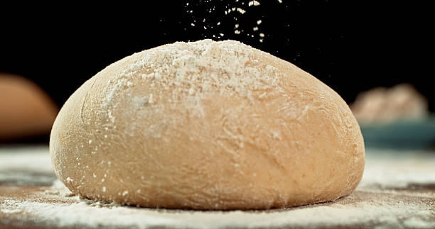 Static shot of a leavened dough loaf isolated on black background with falling flour. Concept of baking, artisan bread making and dough preparation.