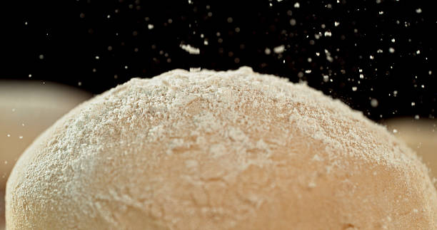 Static shot of a leavened dough loaf isolated on black background with falling flour. Concept of baking, artisan bread making and dough preparation.