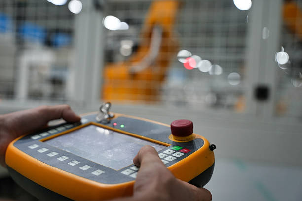 Operator controlling automated robotic system using handheld device in factory environment.