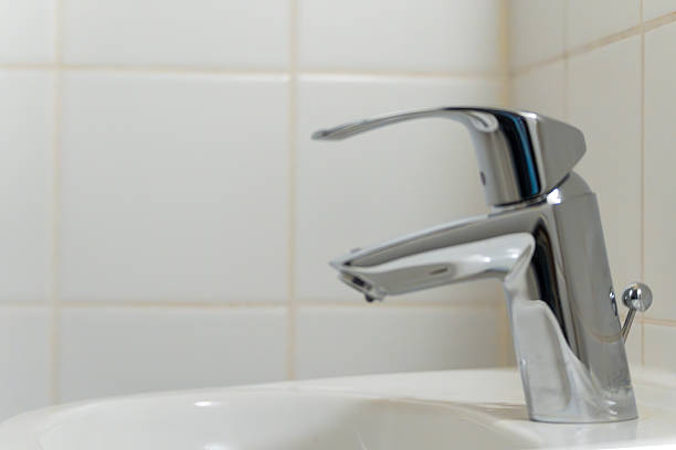 A silver faucet is on a white sink. The faucet is turned off. The sink is clean