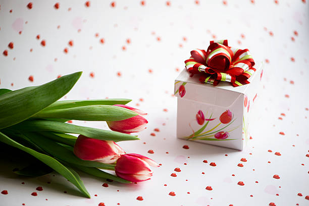 Valentines day composition with red tulips and gift box on a red white hearts  background.