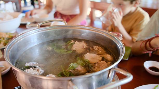 People sharing a hot pot meal during family lunch, cooking fresh ingredients in boiling broth for an authentic asian culinary experience with steam rising