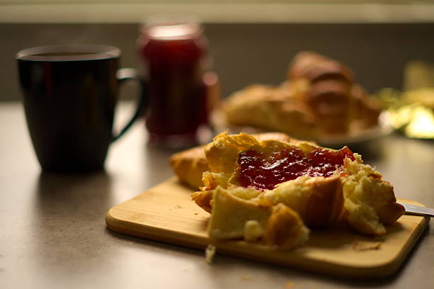 Buttered croissants with jam on a cutting board with cup of hot tea.