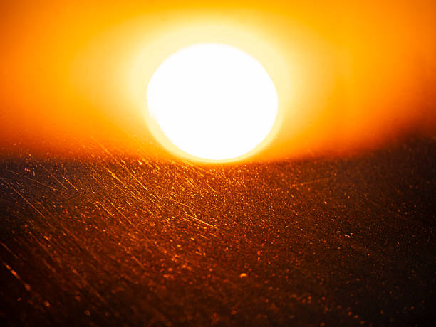 Bright sunset sun low on horizon, reflecting on dusty car window. Warm light, abstract surface texture concept for background.