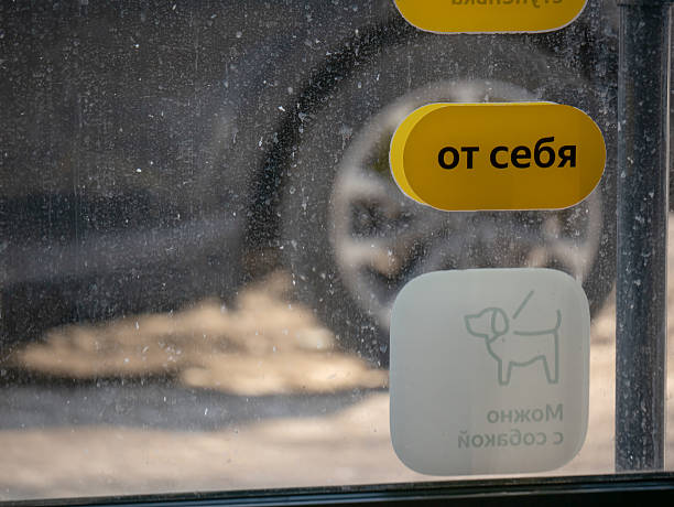 Yellow sign saying pull to open (?? ????) on a dirty window with a dog allowed sticker. Concept of entrance and exit during winter.