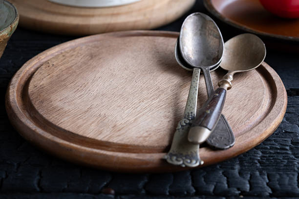 Handcrafted wooden plate with spoon and fork arranged on a dark textured surface. Minimal rustic table setting concept for food presentation, restaurant branding, and natural lifestyle themes.