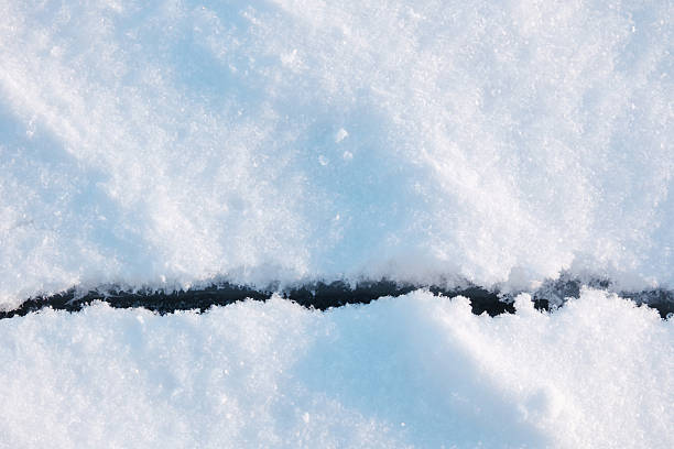 The sunlight emphasizes the sharp contrast between the pristine snow and the dark fissure.