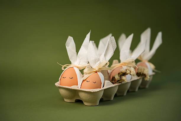 Decorated eggs sit in a carton, shaped like bunny heads. Each egg has a simple design with a bow tied at the top. This scene captures the spirit of Easter crafts.