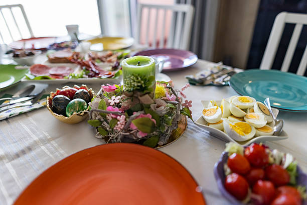 Green candle decorated with a rustic ribbon and surrounded by a floral wreath as part of a festive Easter table setting. Colorful eggs, fresh vegetables, sliced bread, and spring flowers fill the table, creating a bright, celebratory atmosphere for the holiday meal.Shot with Canon R5