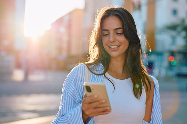 istock Young woman smiling using phone on city street 2261830855