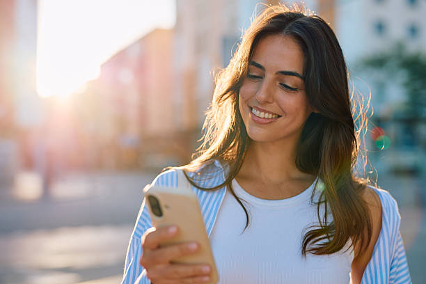 istock Young woman smiling using mobile phone outdoors in city 2261830887