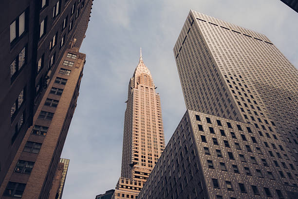 Low angle view of the iconic Chrysler Building framed by surrounding skyscrapers in Midtown Manhattan, New York City. Classic Art Deco architecture against dramatic sky.