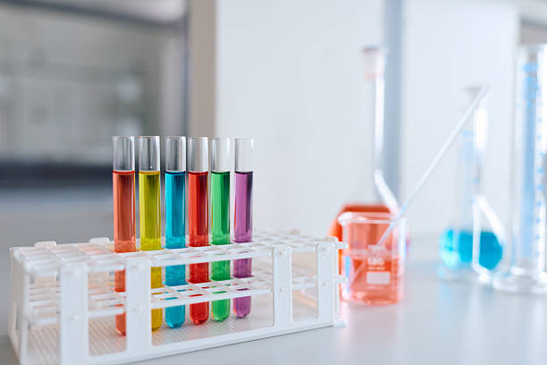 Colorful liquids filling test tubes in a white rack, with beakers and flasks containing various solutions in a bright laboratory environment, symbolizing science, research, and experimentation