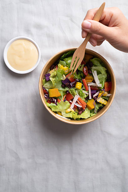 Hand holding fork and eating healthy vegetable salad in takeout bowl with salad dressing