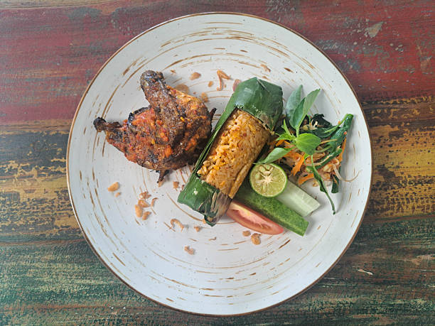 Nasi Bakar or Sticky, fragrant, and spicy grilled rice combined with Ayam Bakar Bumbu Jimbaran Pedas Manis or spicy and sweet Jimbaran-style grilled chicken and fresh vegetables. Indonesia Food Menu. Top View.