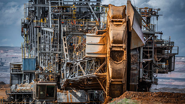 Detailed close-up of a bucket-wheel excavator operating in an open-pit mine. The massive rotating wheel with buckets is actively removing soil and overburden in a large-scale lignite surface mining operation.