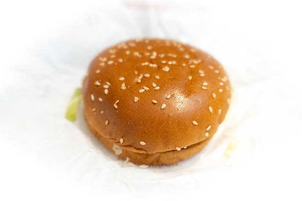 Sesame seed hamburger bun on white paper with lettuce peeking out
