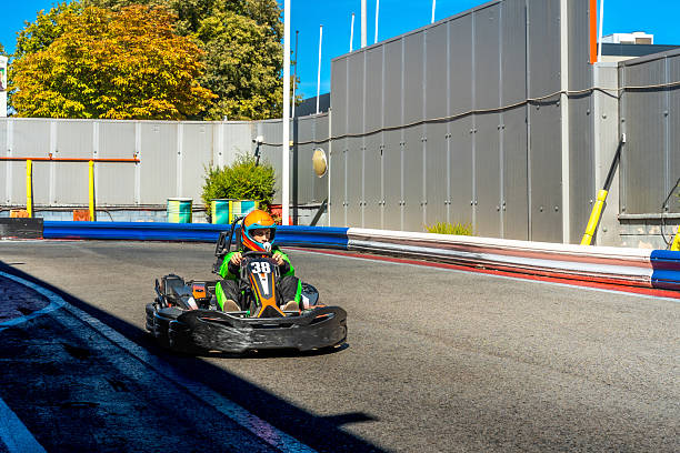 Young boy in helmet and racing suit accelerates a modern go-kart on an outdoor track, focused and thrilled by speed during a sunny, action-packed karting moment